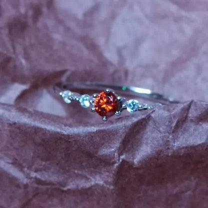 Silberring mit rotem Edelstein und kleinen Diamanten auf braunem Hintergrund.