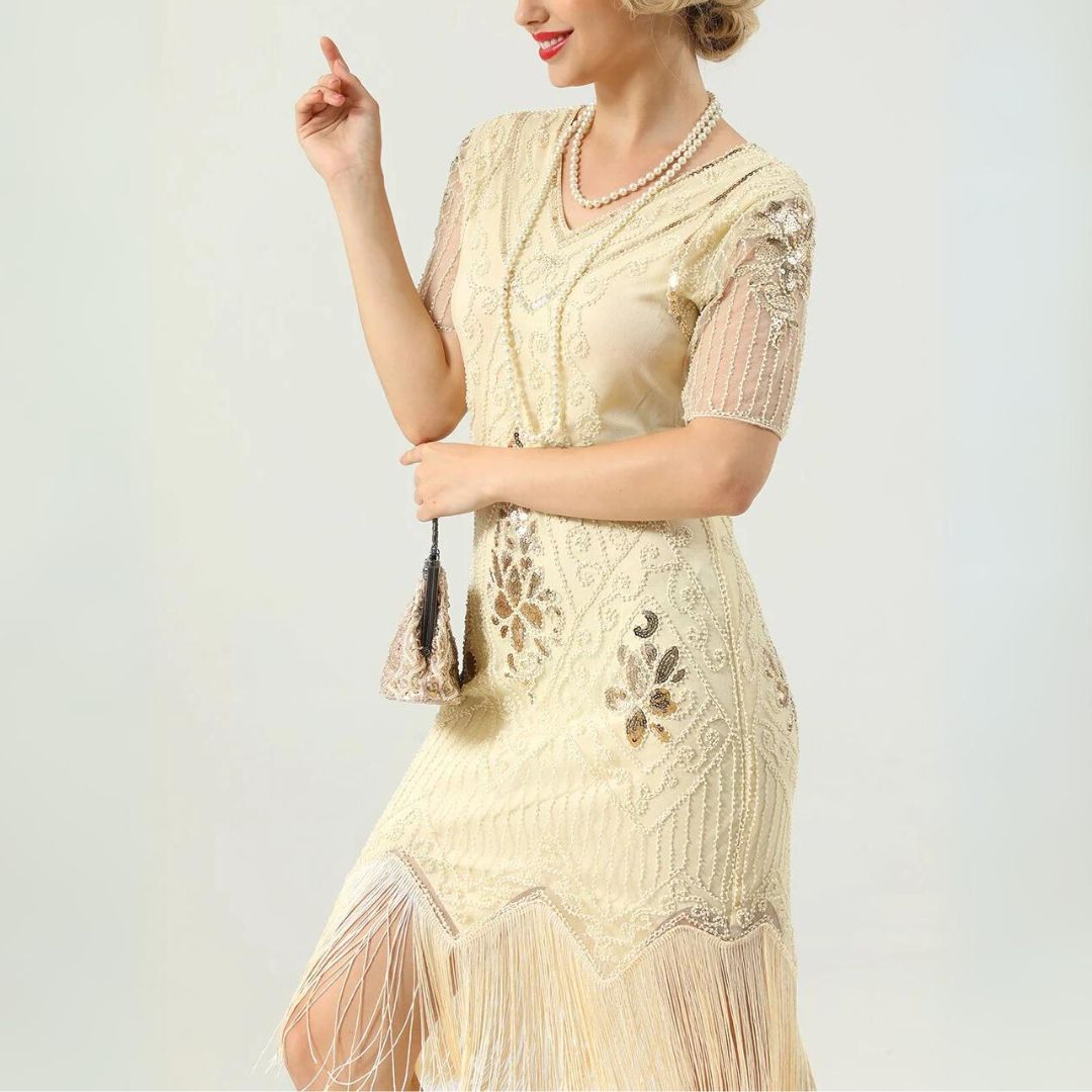 Frau in cremefarbenem, besticktem Fransen-Kleid im Vintage-Stil mit Perlenkette.