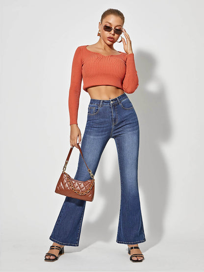 Frau in blauer Schlagjeans und orangefarbenem Oberteil, trägt braune Handtasche und Sonnenbrille.