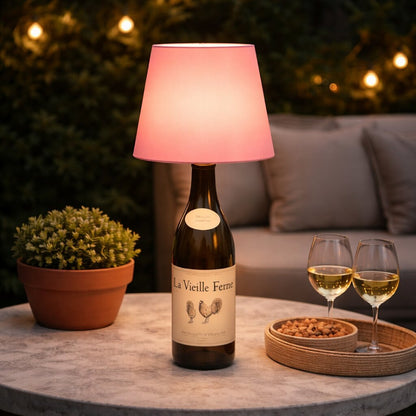 Lysande rosa flasklampa på en brun vinflaska på ett utebord med vitvinsglas och nötter 19