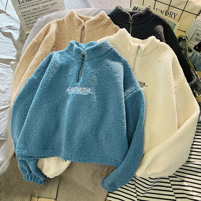 Vier Fleece-Pullover mit Reißverschluss in Blau, Beige, Weiß und Schwarz auf einem Tisch.