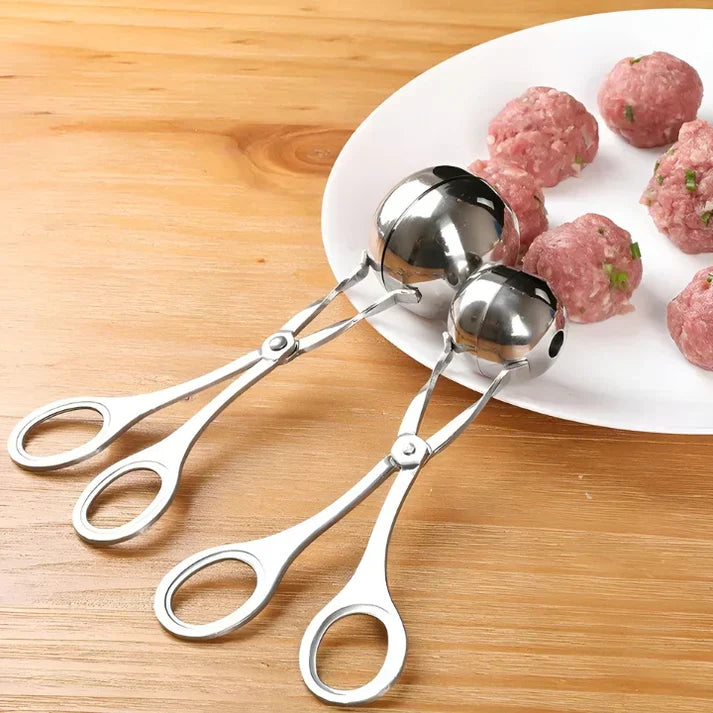 Fleischbällchenformer aus Edelstahl auf Holztisch neben Teller mit rohen Fleischbällchen.
