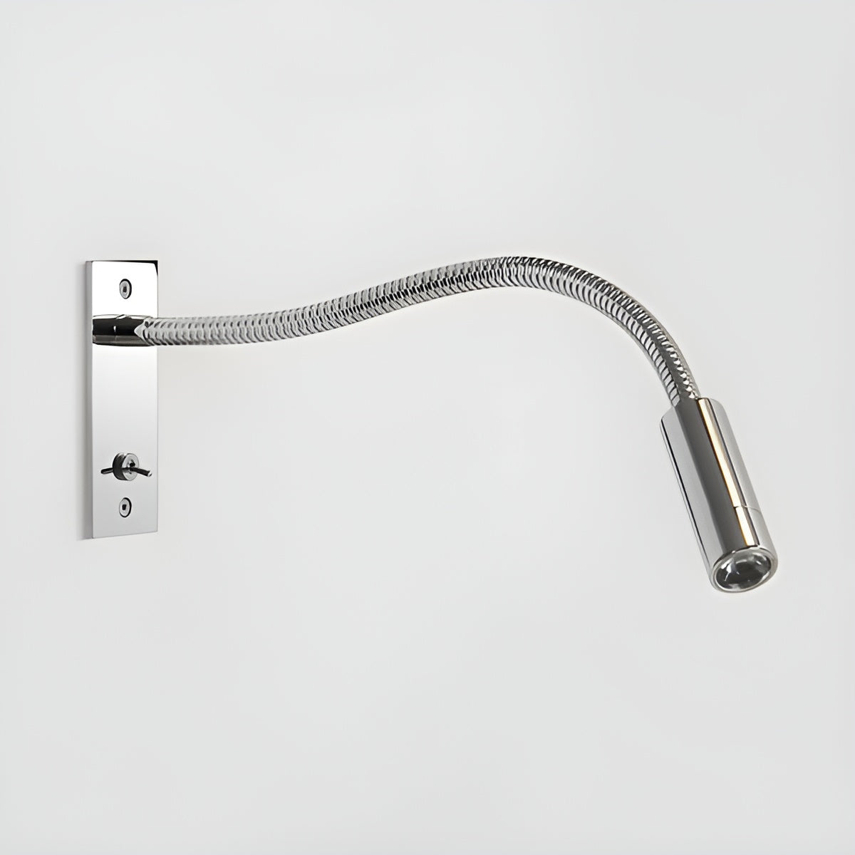 Vägglampa i blank krom med flätad böjlig arm, tippströmbrytare på väggplattan och cylinderformat lamphuvud. 12