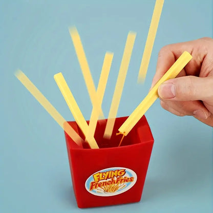Rotes Spielzeug mit fliegenden Pommes, Hand wirft gelbe Stäbchen, blauer Hintergrund.