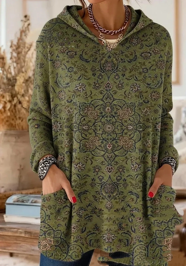 Grön huvtunika med tätt blommigt orientaliskt mönster i mörkblått och rosa, buren av modell med händerna i framfickorna. 7