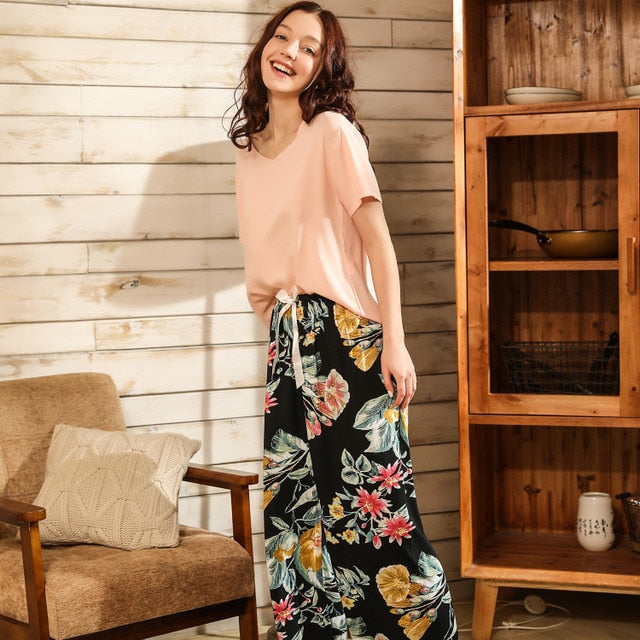 Frau in rosa T-Shirt und floraler Hose, lächelnd im Wohnzimmer, moderne Freizeitmode.