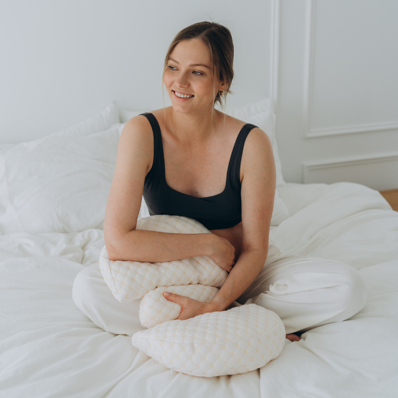 Frau auf Bett mit ergonomischem Stillkissen, weiß, bequem, für Mütter, Stillhilfe, Schlafzimmer.