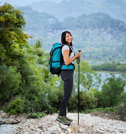 Frau mit grünem Wanderrucksack und Trekkingstöcken in bergiger Landschaft.