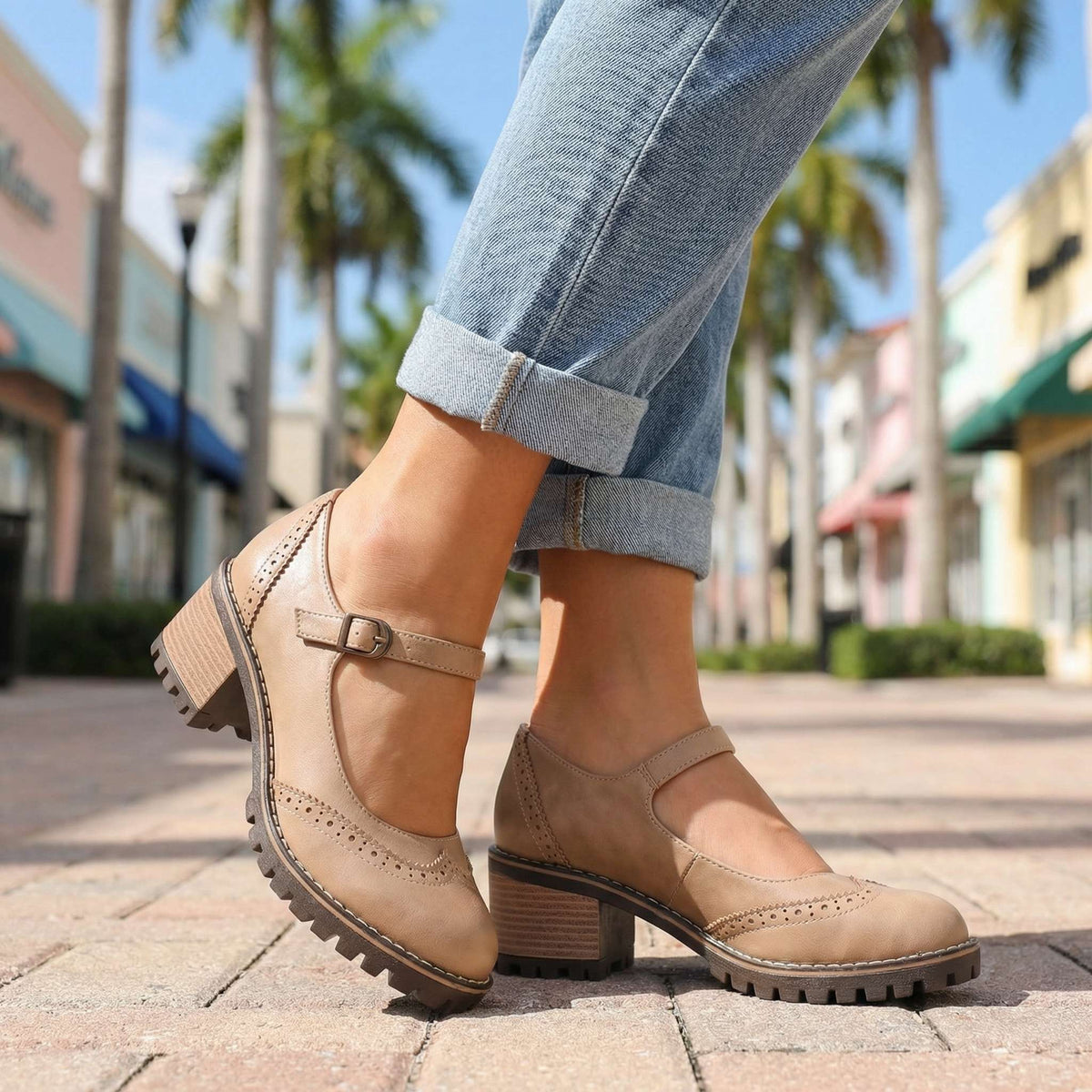 Beige Mary Jane-skor med brogue-mönster och spänne, bärs med uppvikta jeans på en stenlagd gata med palmer. 6
