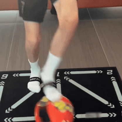 Person jongliert mit rotem Fußball auf schwarzer Matte, trägt weiße Socken und schwarze Shorts.