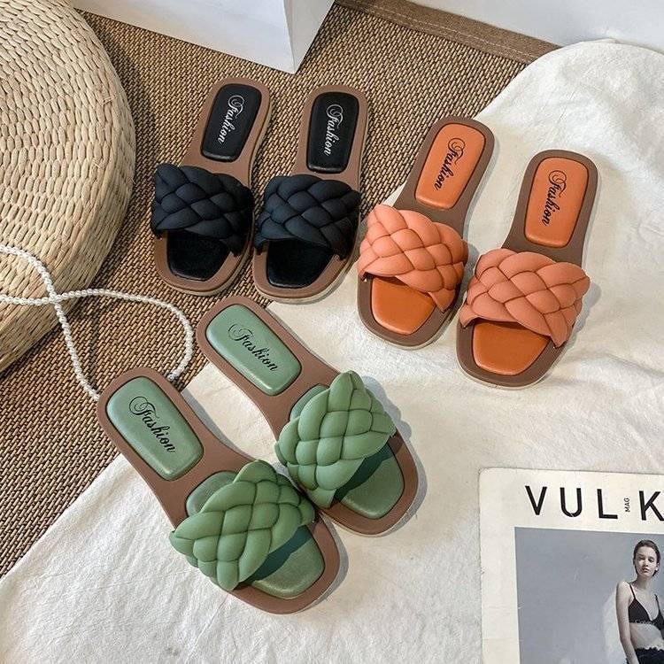 Geflochtene Damen-Sandalen in Schwarz, Orange und Grün auf Teppich, modische Sommerschuhe.