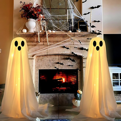 Zwei leuchtende Geisterdekorationen vor Kamin, Halloween-Deko, Spinnweben, Kürbisse.