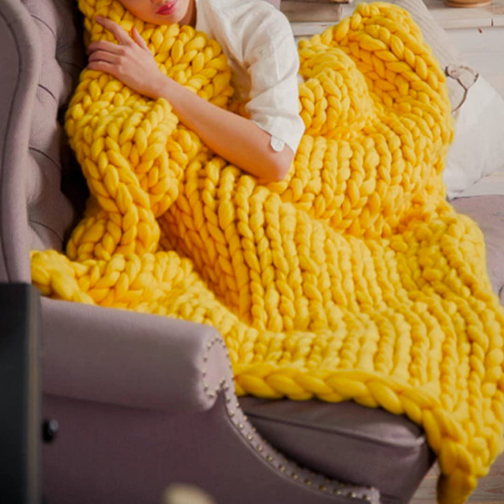 Frau mit gelber, grob gestrickter Decke auf Sofa, gemütlich, Wohnzimmer, Entspannung.