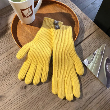 Gelbe Strickhandschuhe aus Wolle auf Holztisch neben Kaffeetasse und Autopostkarte.
