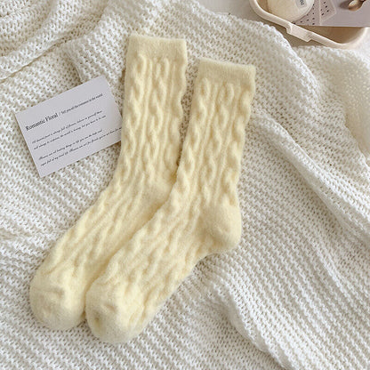 Gelbe Wollsocken mit Zopfmuster auf weißem Strickhintergrund, gemütliche Wintermode.
