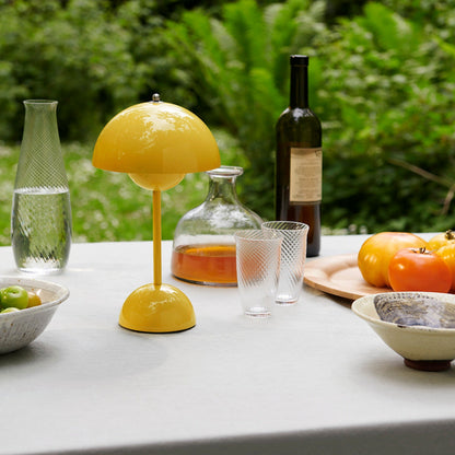 Gelbe Tischlampe auf Gartentisch mit Gläsern, Karaffe, Flasche und frischen Tomaten.