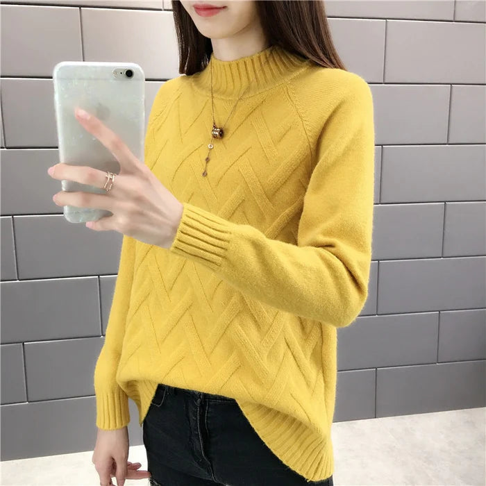 Frau in gelbem Strickpullover mit hohem Kragen, Smartphone, graue Kacheln, Wintermode.