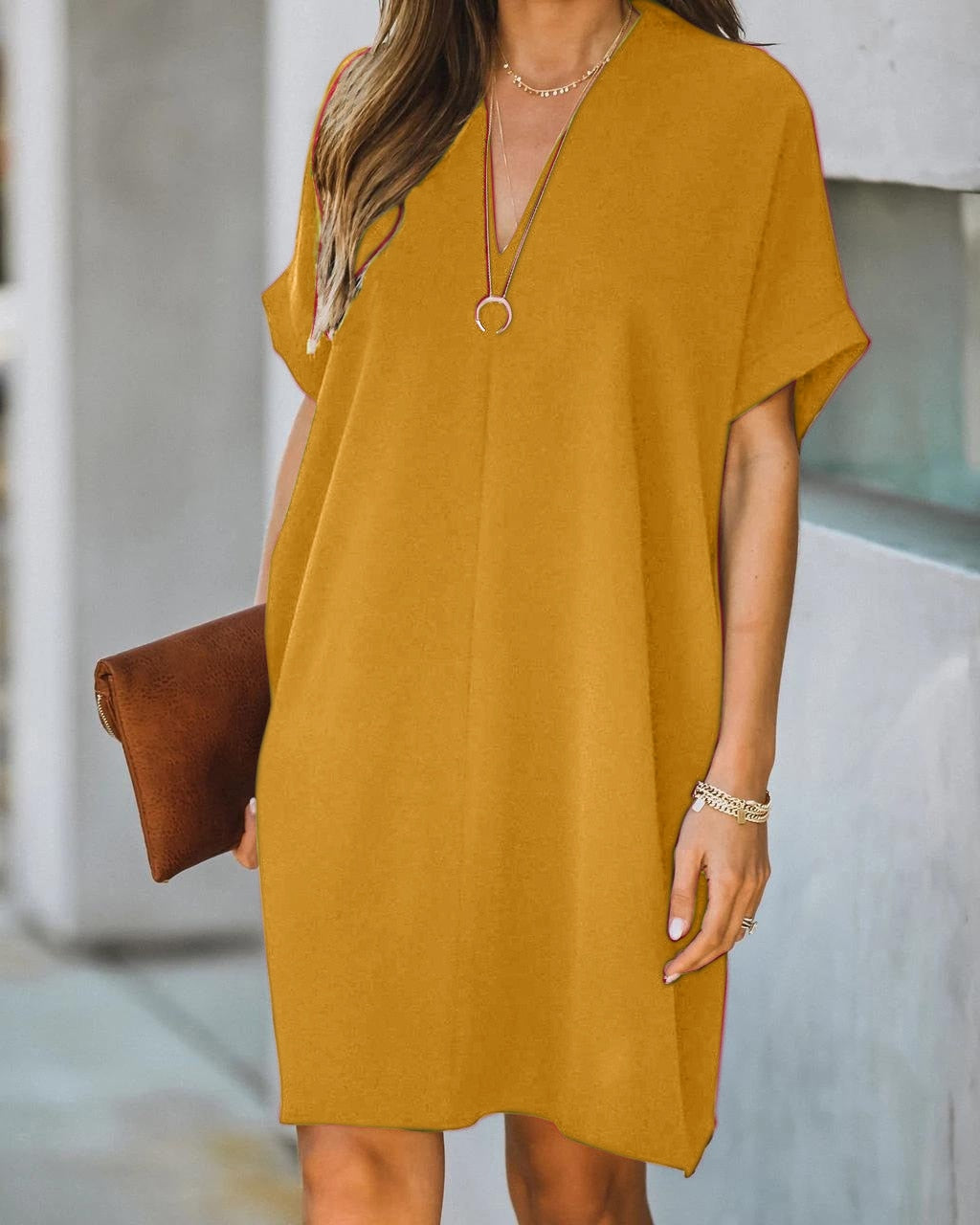 Frau in senfgelbem Sommerkleid mit V-Ausschnitt, brauner Clutch, lässiger Stil.