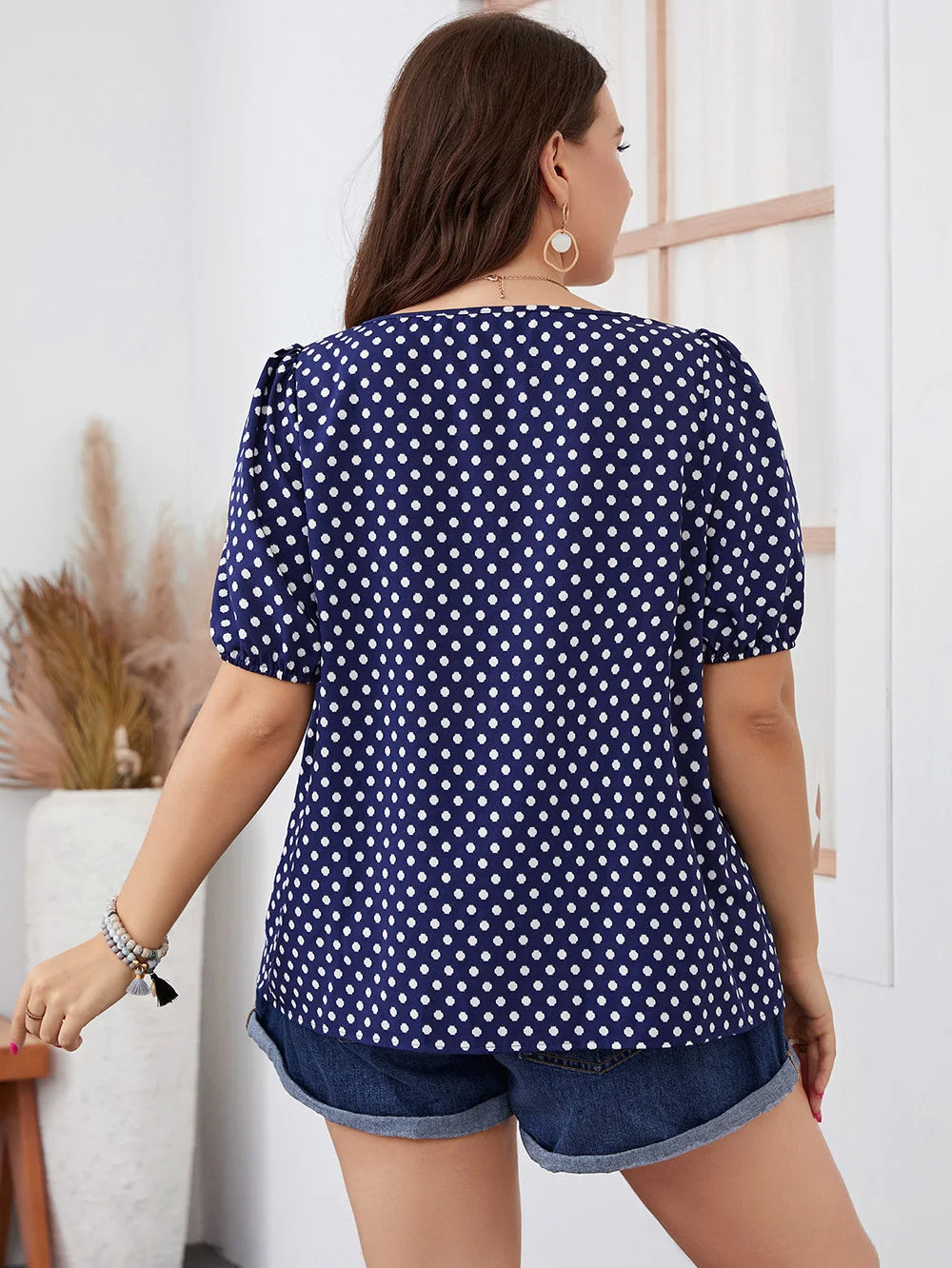 Frau in blauer gepunkteter Bluse und Jeansshorts, Rückansicht, lässige Sommermode.