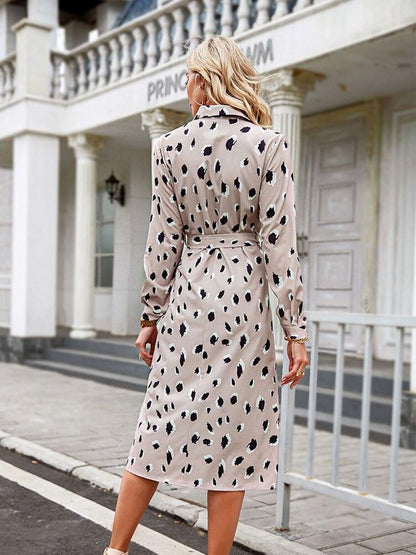 Frau in beigem, gepunktetem Kleid, Langarm, knielang, vor historischer Architektur.