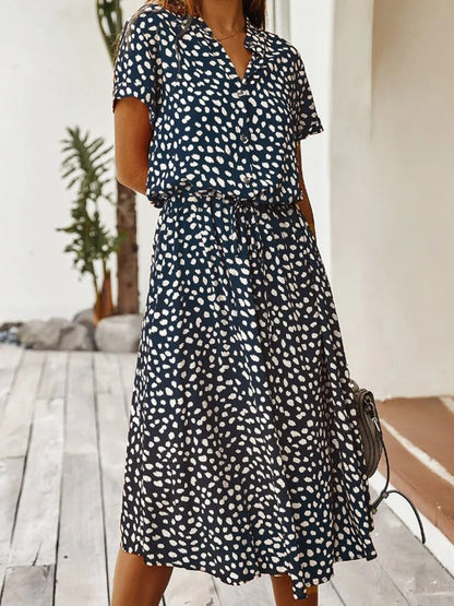 Frau in blau-weiß gepunktetem Sommerkleid, knielang, kurzärmelig, modisch, draußen.