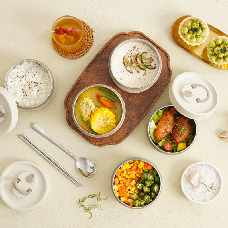 Mehrere Bento-Boxen mit Reis, Gemüse, Suppe und Getränk auf hellem Tisch.