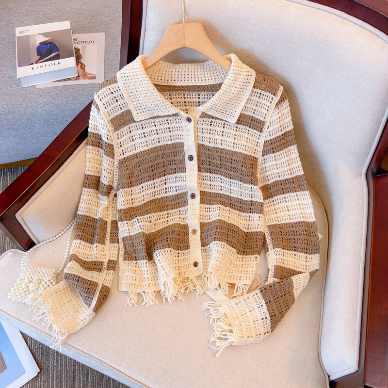 Gestreifte Häkel-Strickjacke, beige und braun, mit Fransen, auf einem Sessel liegend.