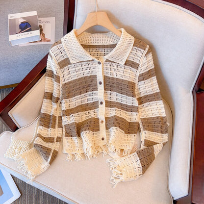 Gestreifte Häkel-Strickjacke, beige und braun, mit Fransen, auf einem Sessel liegend.