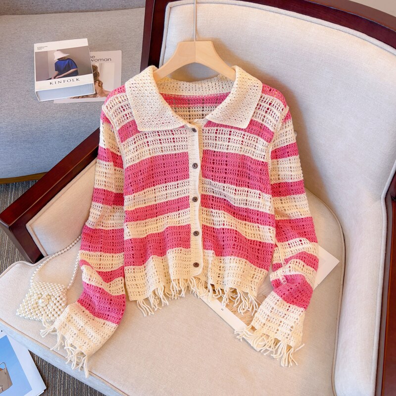 Gestreifte Strickjacke in Rosa und Weiß, gehäkelt, mit Fransen, auf einem Sessel drapiert.
