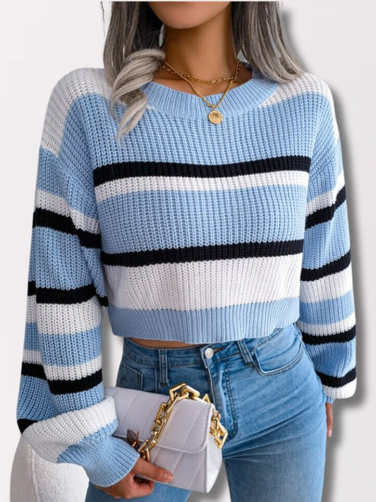 Frau in blau-weiß gestreiftem Strickpullover, Jeans, hält weiße Tasche mit goldener Kette.