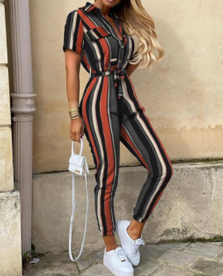 Frau in gestreiftem Jumpsuit, rot-schwarz-beige, mit weißer Handtasche und Sneakers.