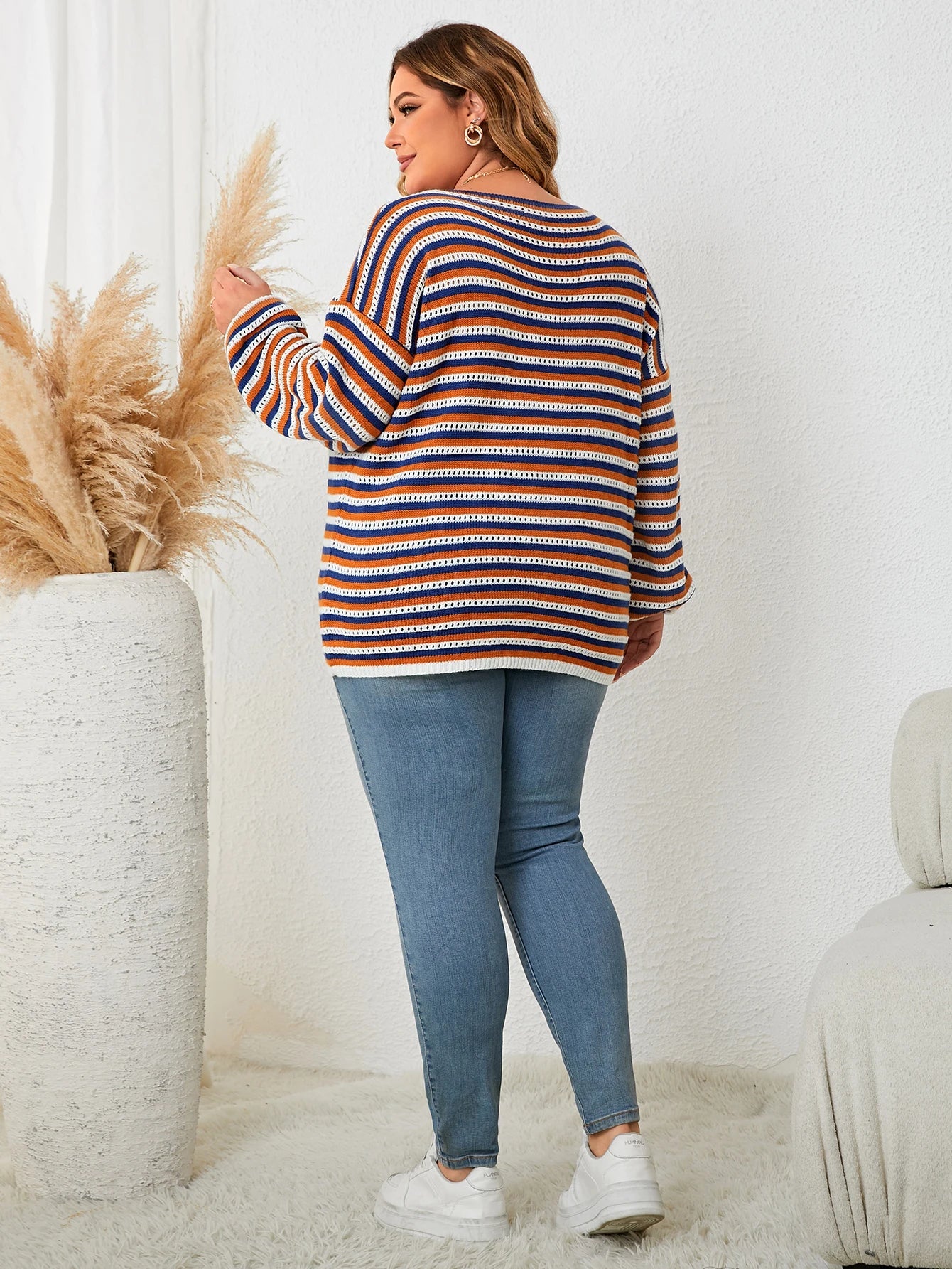 Frau in gestreiftem Pullover und Jeans, steht neben Pampasgras, lässige Mode, gemütliches Outfit.