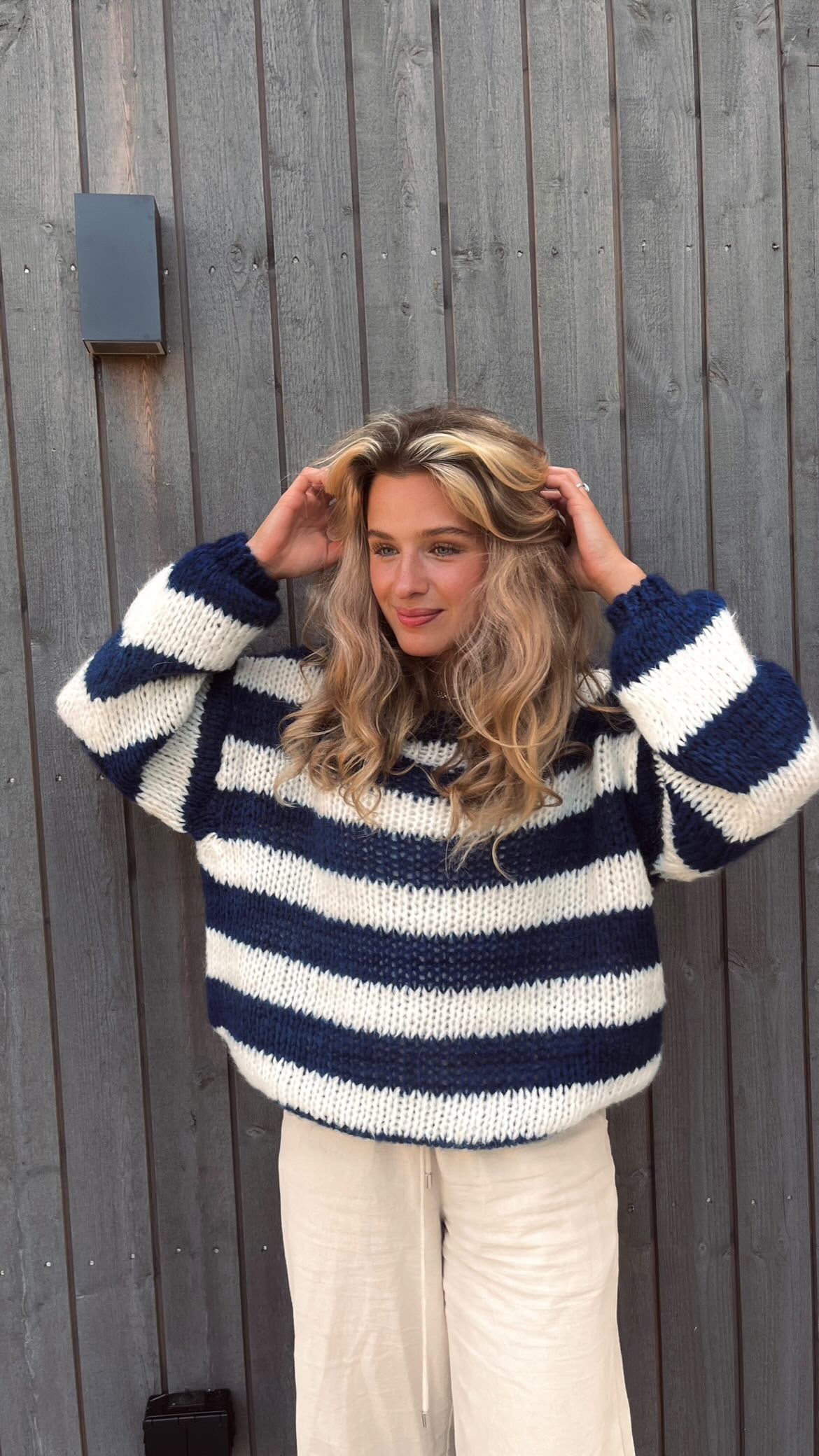 Frau in gestreiftem Pullover vor Holzwand, blau-weiß, lässige Mode, Herbstoutfit.