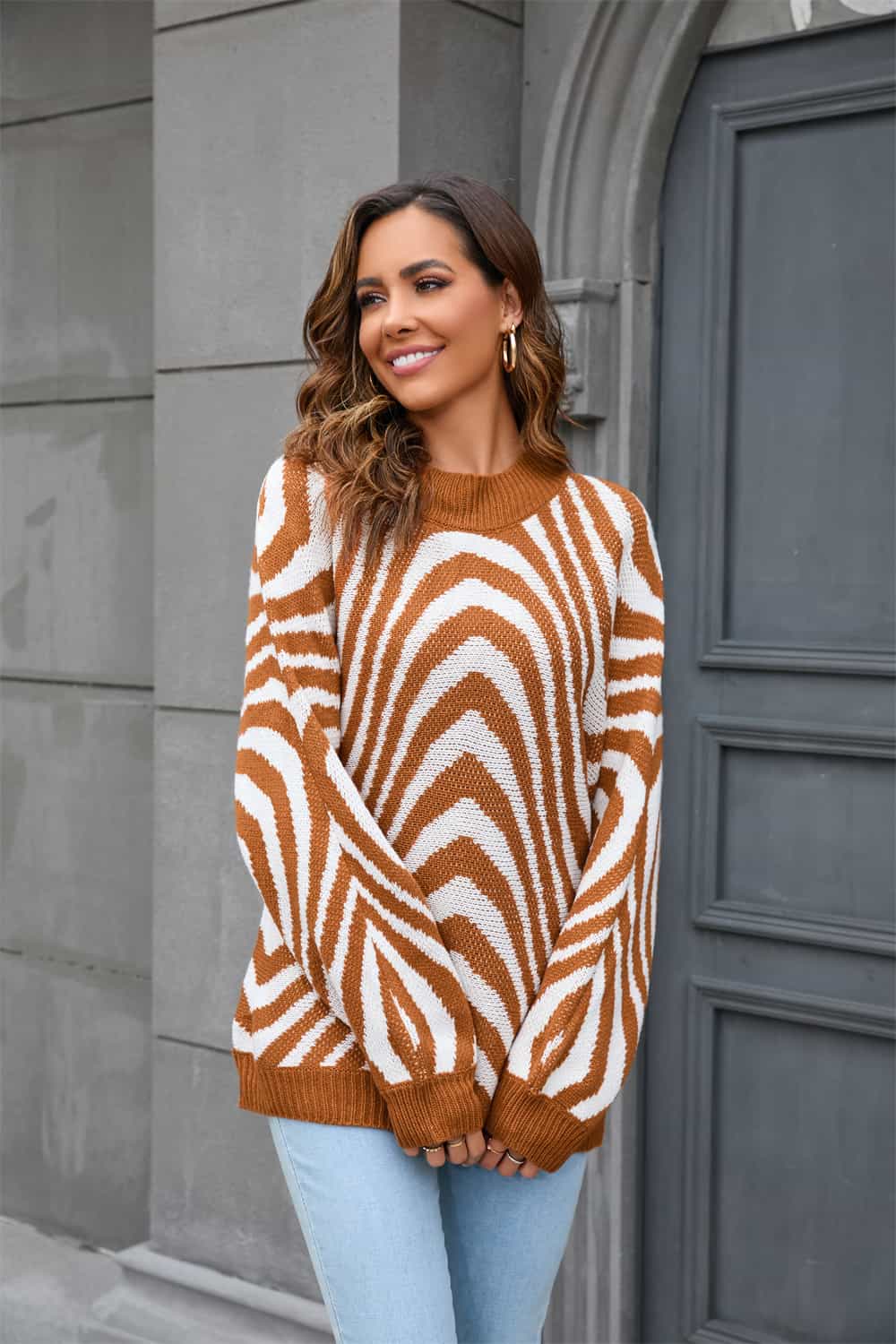 Frau in braun-weiß gestreiftem Pullover, lächelnd, vor grauer Wand, modisch, Herbstmode.