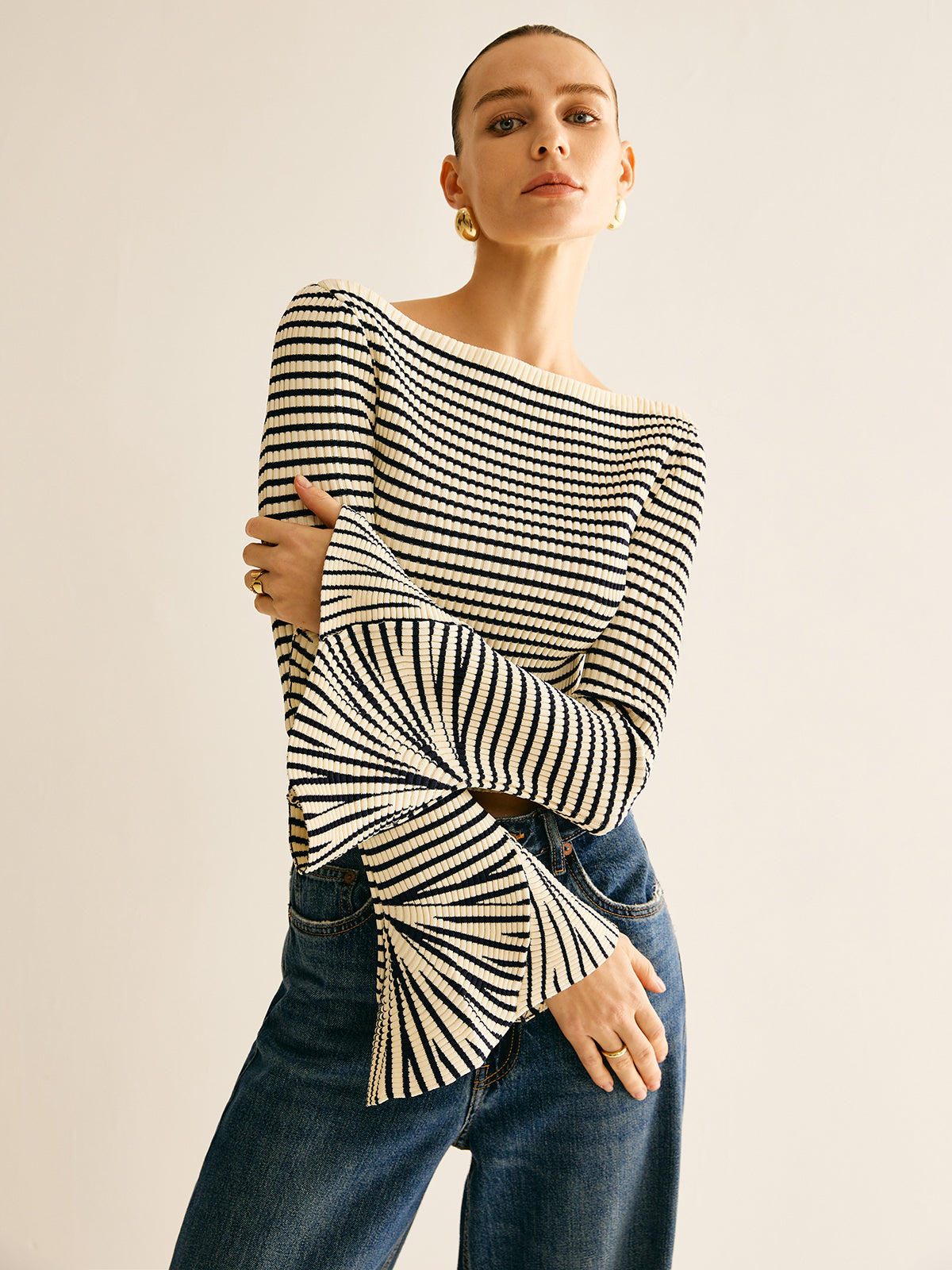 Frau in gestreiftem Pullover mit Trompetenärmeln und blauer Jeans, modisch, elegant.