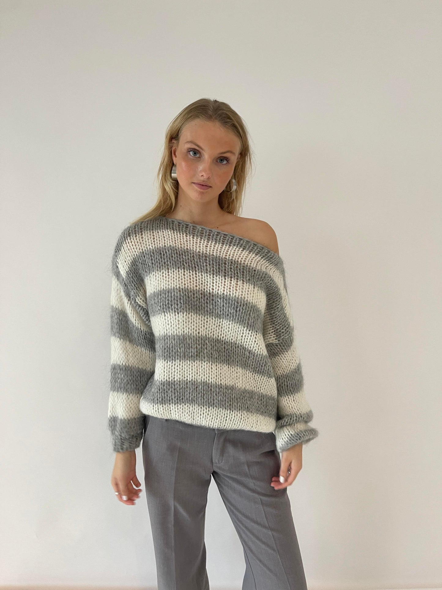 Frau in gestreiftem Pullover und grauer Hose vor weißem Hintergrund, modisch, lässig.