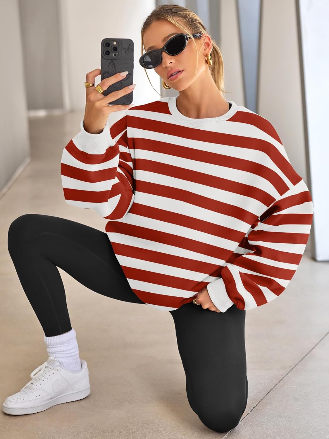 Frau in rot-weiß gestreiftem Pullover, schwarze Leggings, Sonnenbrille, Smartphone, modern.