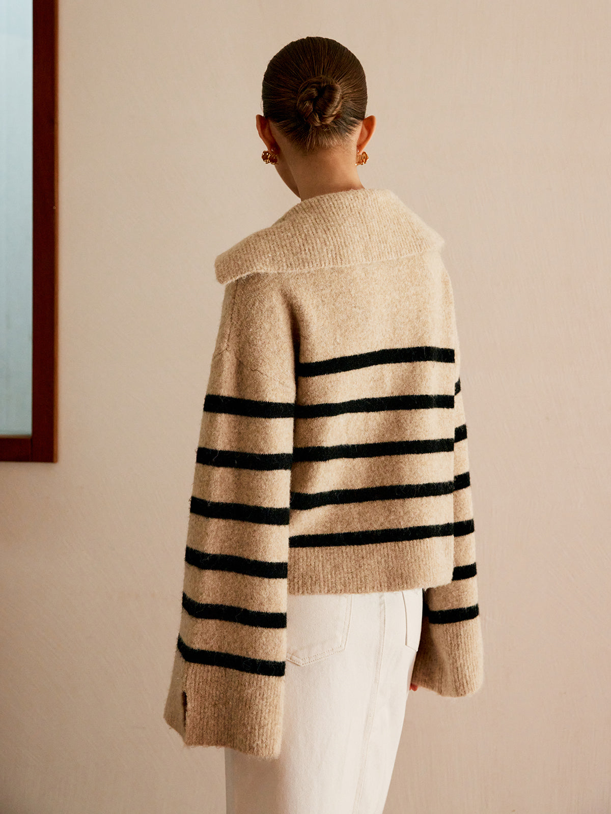 Frau in gestreiftem Pullover, beige mit schwarzen Streifen, Rückansicht, modisch, elegant.