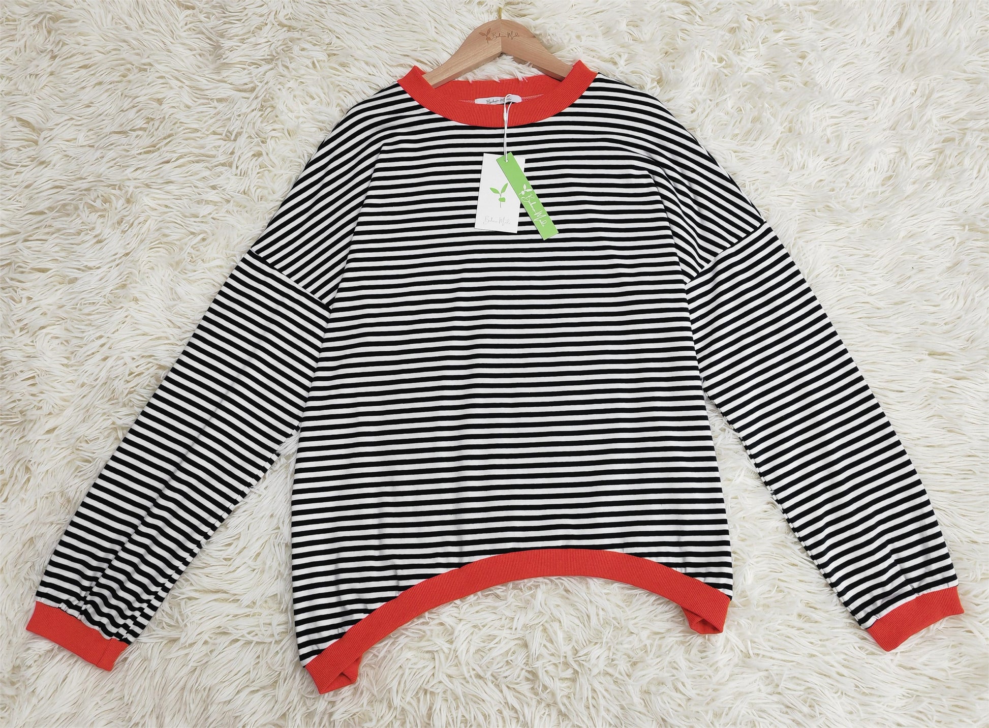 Schwarz-weiß gestreifter Pullover mit roten Bündchen auf weißem Teppich.