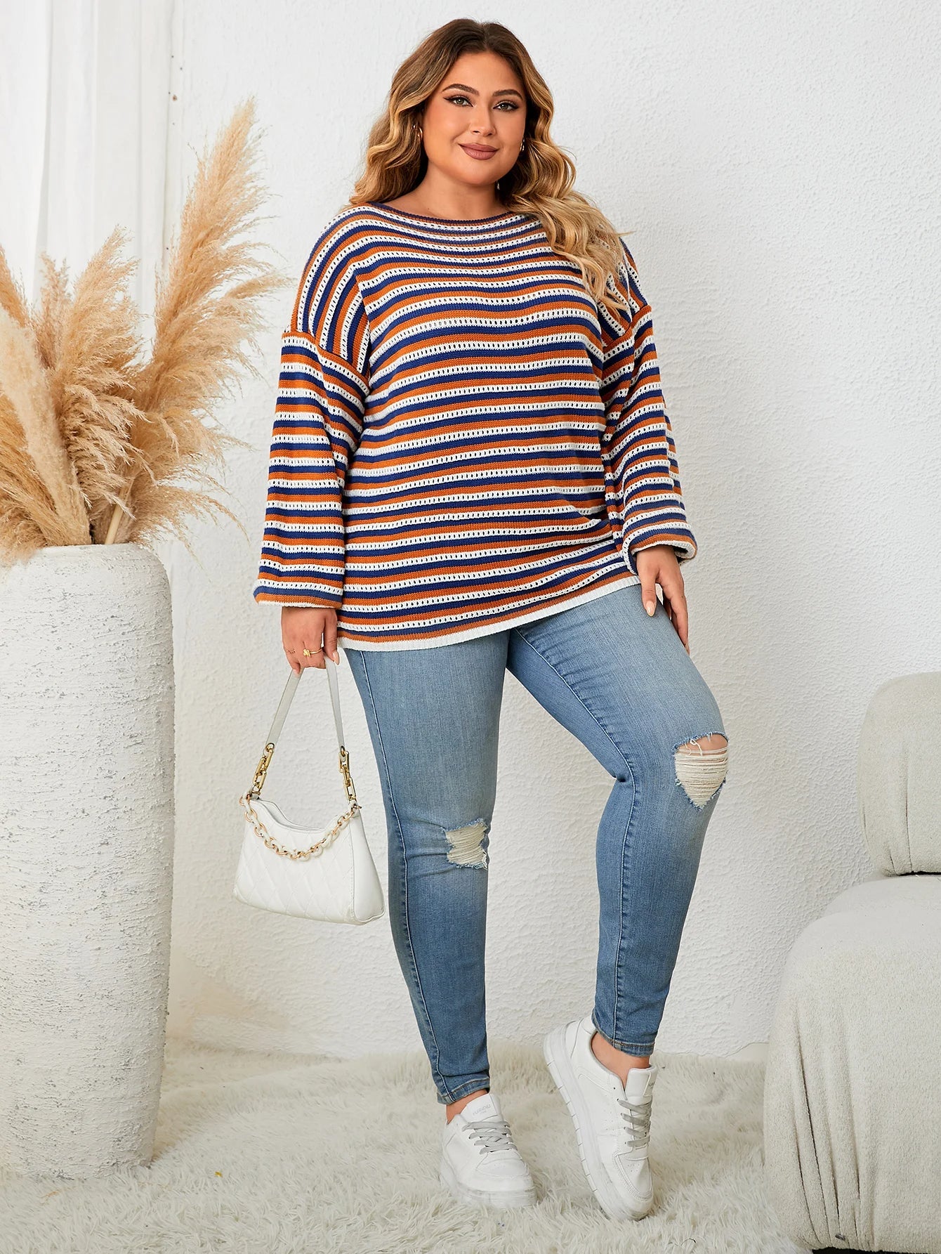 Frau in gestreiftem Pullover, zerrissene Jeans, weiße Sneaker, hält weiße Handtasche.