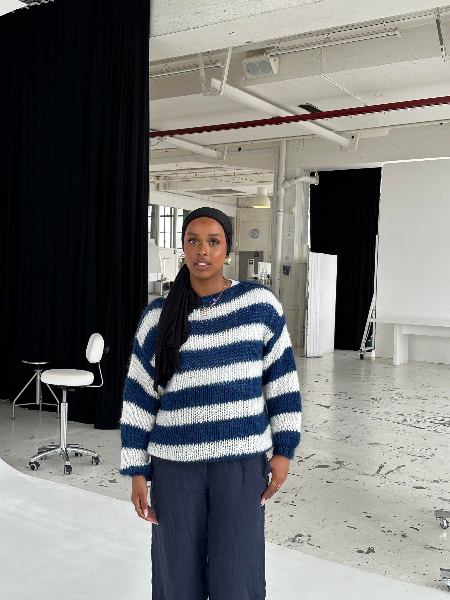 Frau in gestreiftem Pullover und dunkler Hose in modernem Fotostudio.