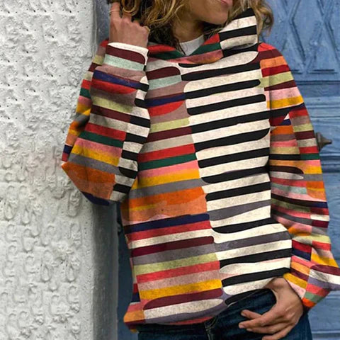 Frau in gestreiftem, buntem Hoodie vor blauer Tür und weißer Wand.