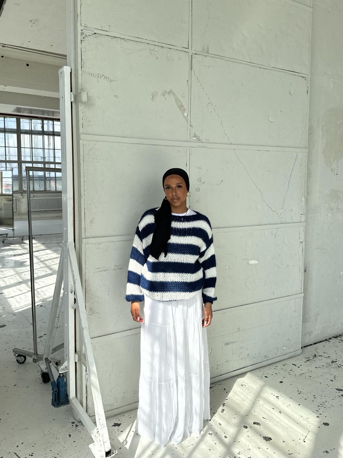 Frau in gestreiftem Pullover und weißem Rock in hellem, industriellem Raum.