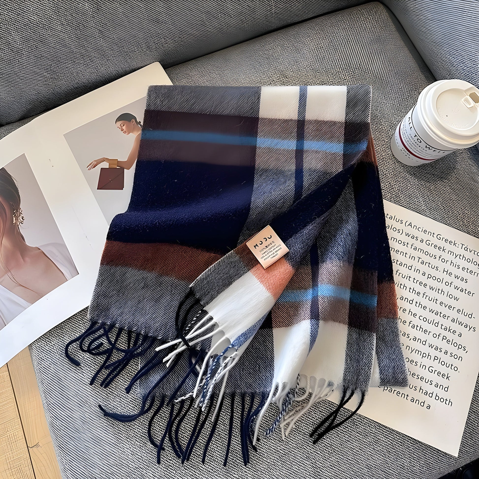 Gestreifter Wollschal in Blau, Weiß und Braun auf grauem Sofa, neben Kaffeebecher und Magazin.