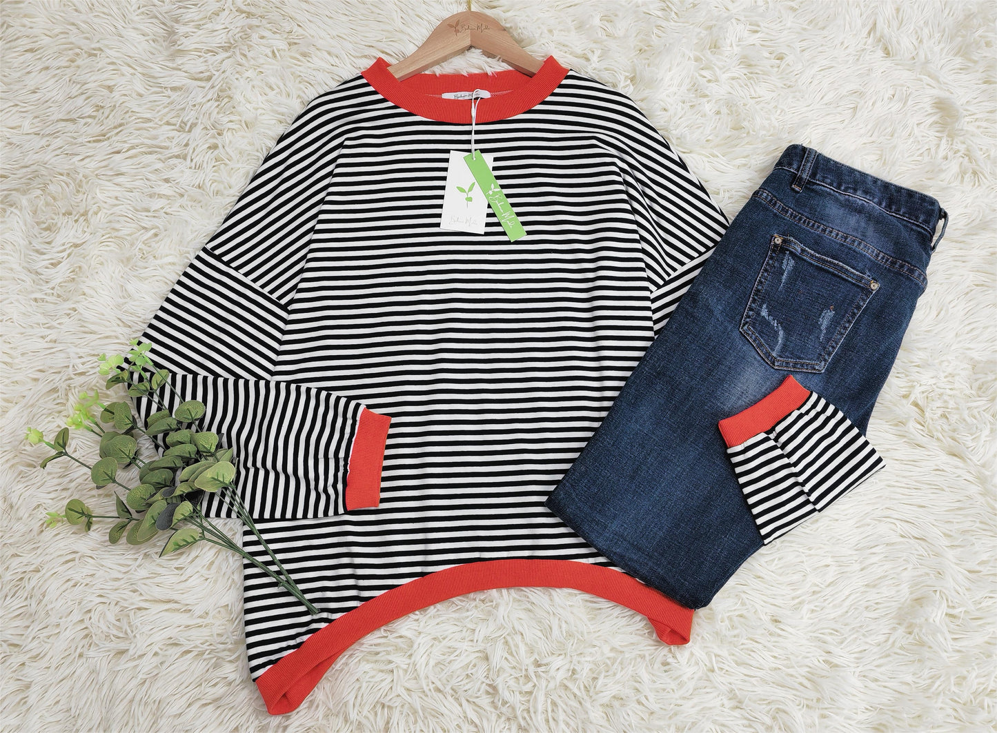 Gestreiftes Langarmshirt mit roten Bündchen und blaue Jeans auf weißem Teppich.