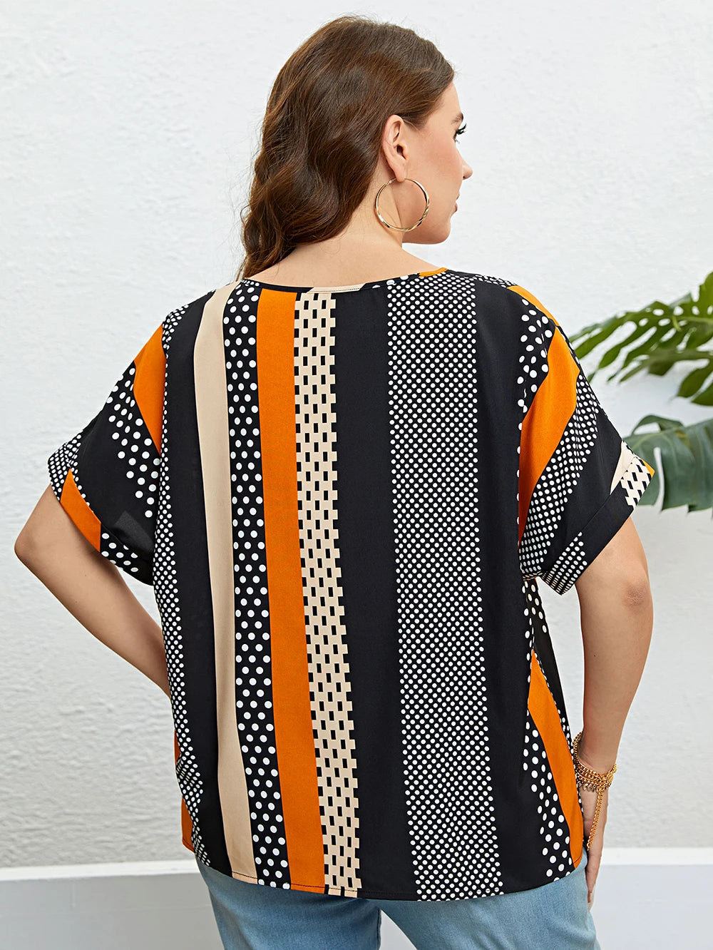 Frau trägt gestreiftes, gepunktetes T-Shirt in Schwarz, Orange und Beige, Rückansicht.