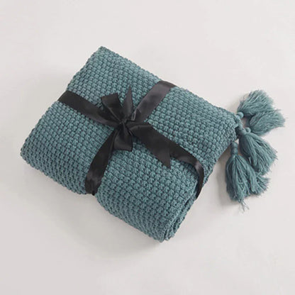 Gefaltete blaue Strickdecke mit schwarzer Schleife und Quasten, gemütliche Wohnaccessoires.