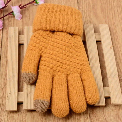Gelbe gestrickte Winterhandschuhe mit Touchscreen-Funktion auf Holzuntergrund.
