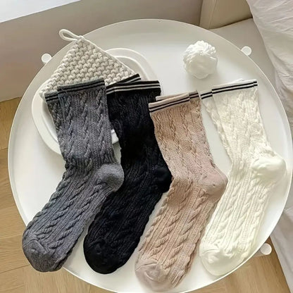 Vier Paar gestrickte Socken in Grau, Schwarz, Beige und Weiß auf einem weißen Tisch.