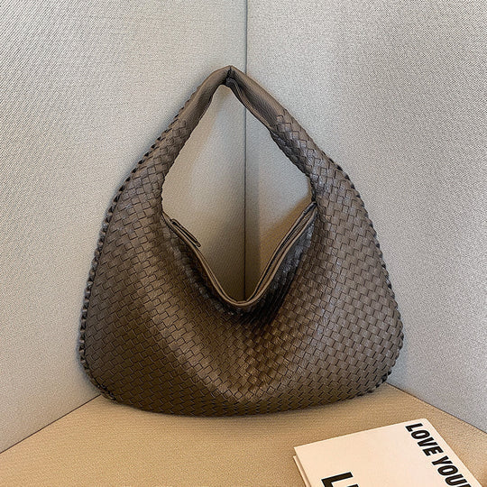 Geflochtene braune Handtasche aus Leder auf Sofa, modisch, elegant, Damenaccessoire.